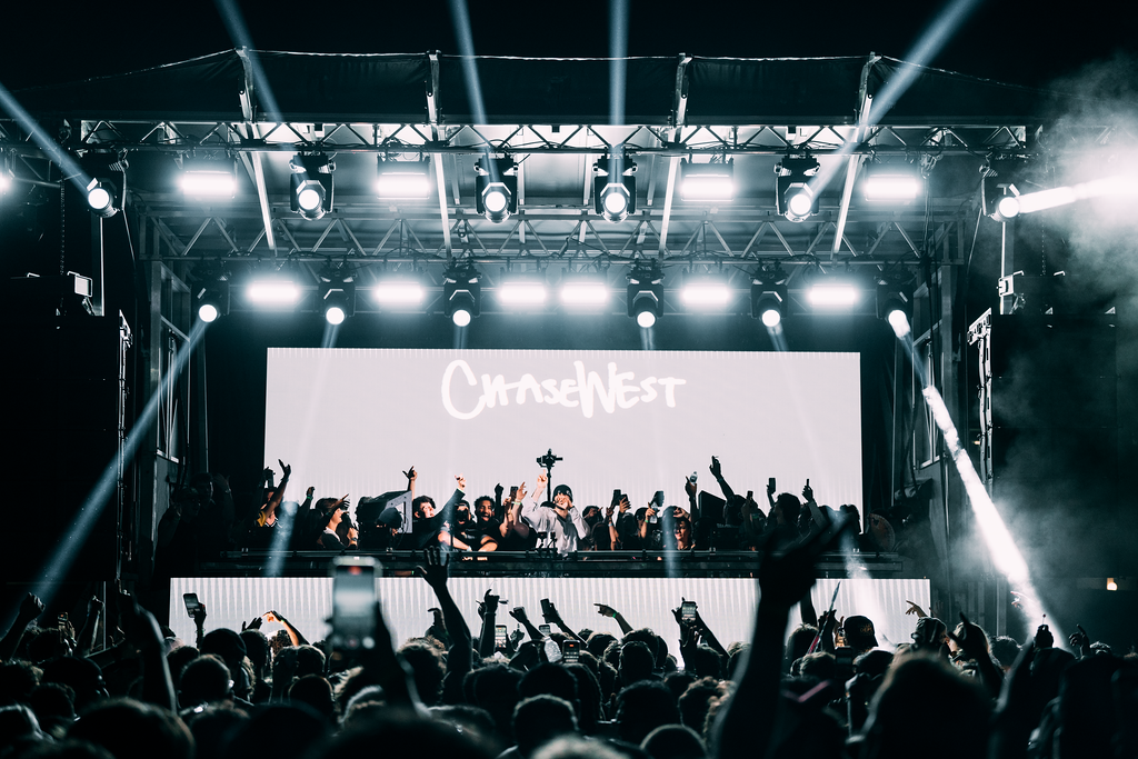 | JPC Entertainment Crowd at a nighttime concert facing a large illuminated stage with a digital screen showing 'ChaseNest' and hands raised in the air.